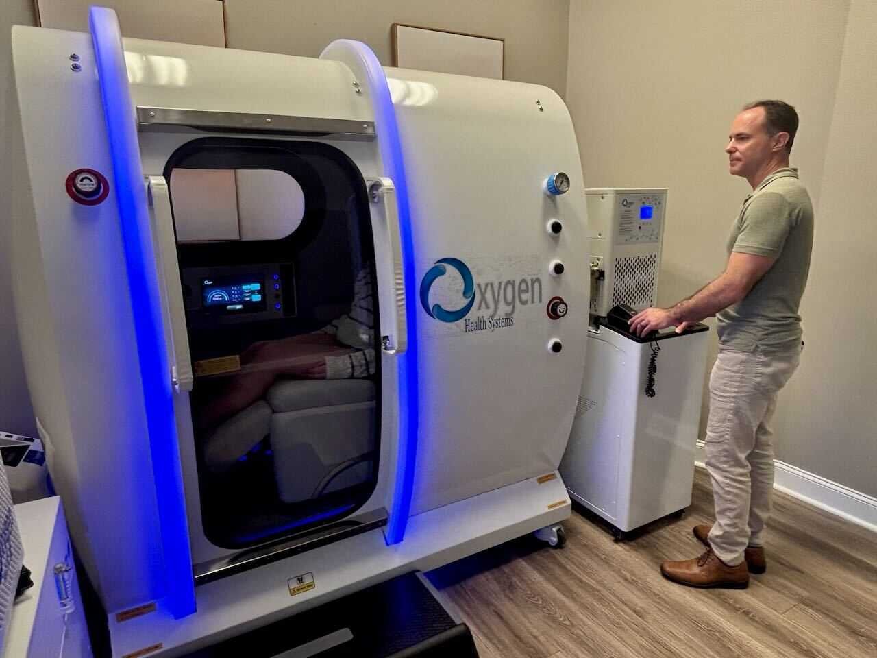 A sunlit, modern neurofeedback clinic in Wake Forest featuring ergonomic chairs with advanced headsets, a clinician warmly greeting a client with brainwave data on a tablet, polished wood floors, fresh greenery, and subtle details, creating a tranquil, welcoming atmosphere for personalized wellness services.